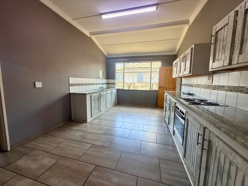 A functional kitchen featuring built-in cabinetry, stone countertops, an integrated oven and hob, and tiled flooring with a neutral color palette.