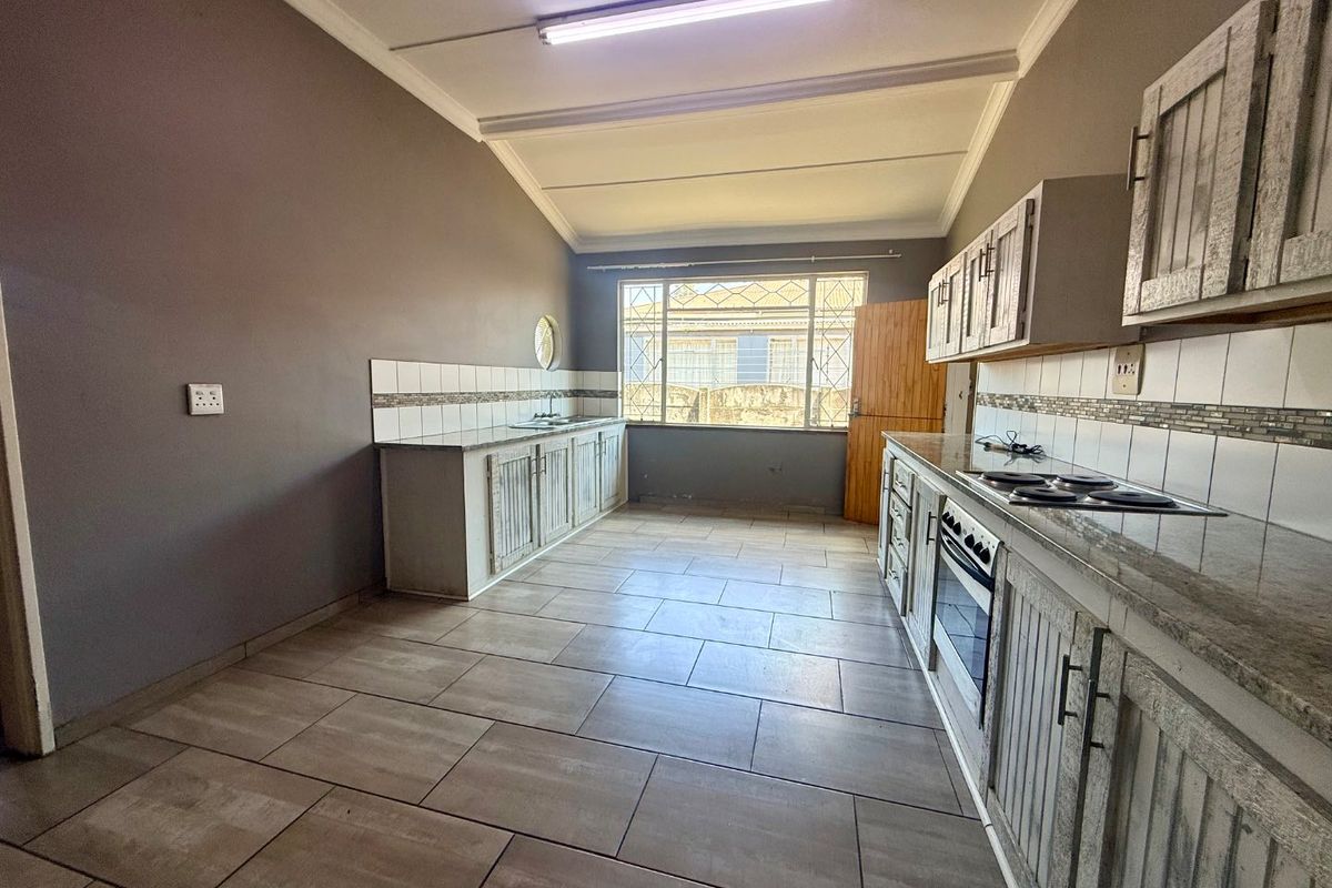 A functional kitchen featuring built-in cabinetry, stone countertops, an integrated oven and hob, and tiled flooring with a neutral color palette.
