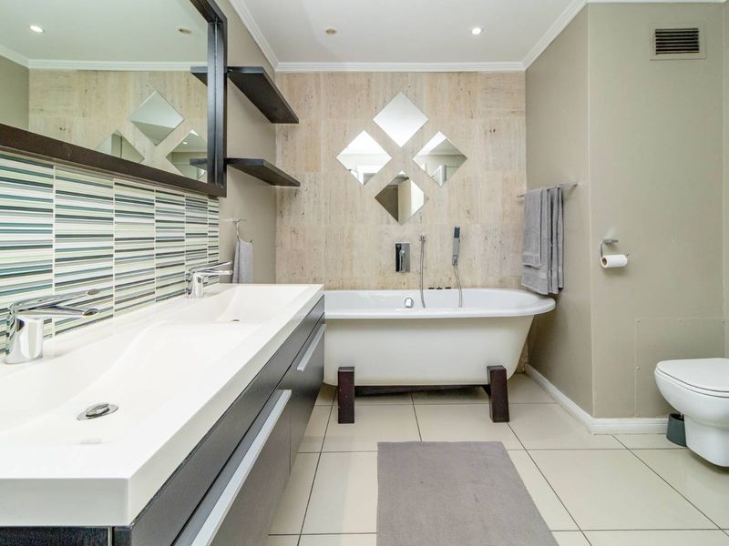 Modern bathroom featuring a double vanity, a freestanding bathtub, wall-mounted toilet, and elegant stone wall accents with contemporary tile finishes.