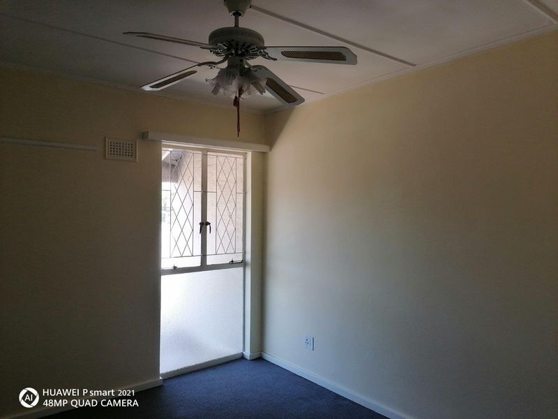 An empty bedroom featuring a ceiling fan, carpeted flooring, and a security gate over the window.