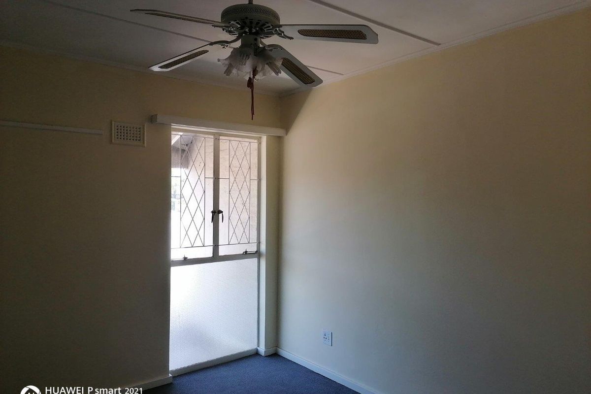 An empty bedroom featuring a ceiling fan, carpeted flooring, and a security gate over the window.