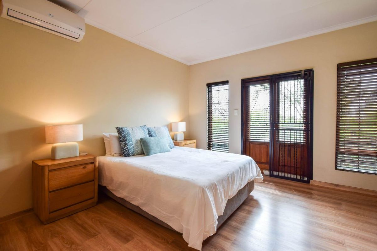 A well-maintained bedroom featuring laminate flooring, a wall-mounted air conditioning unit, and direct access to the outdoors through a timber-framed glass door.