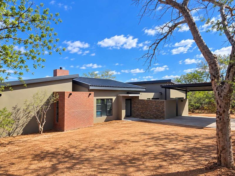 Modern single-story house featuring a combination of brick and stone cladding, a metal roof, and an integrated carport set in a natural landscape.