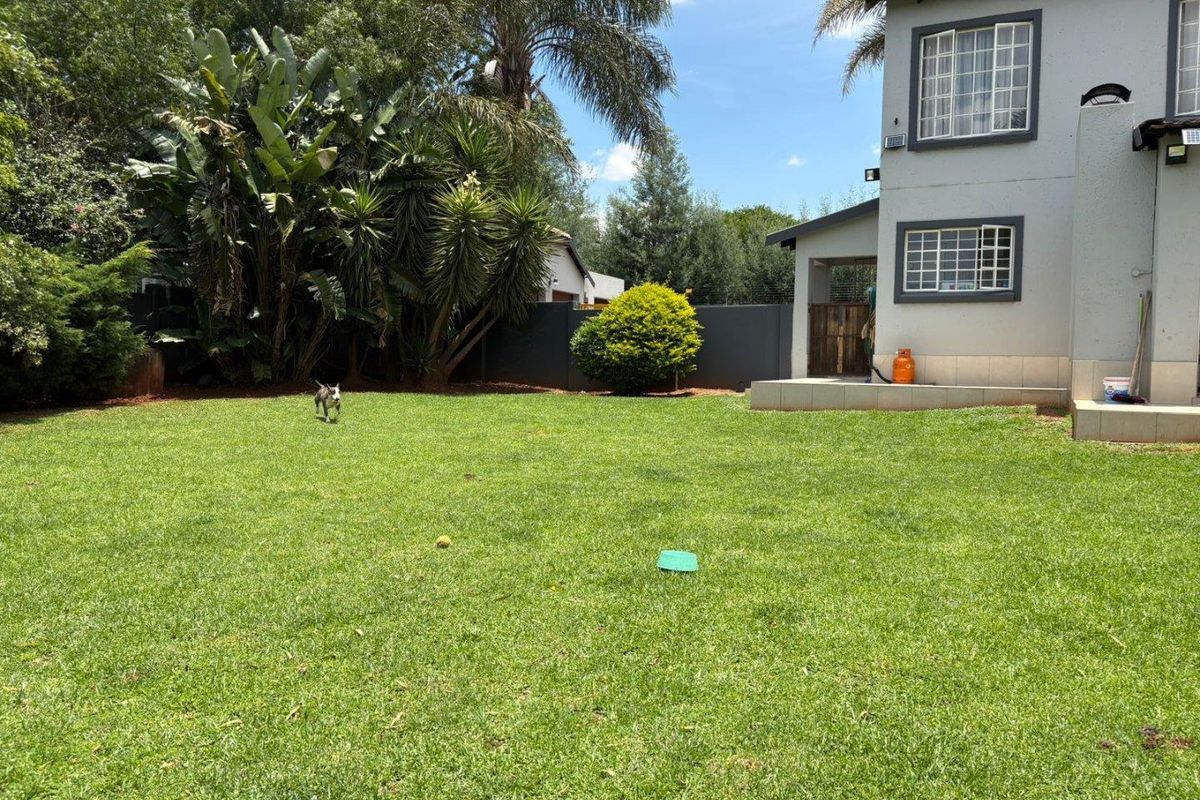 A spacious rear garden featuring a well-maintained lawn, boundary wall, and a small tiled patio area attached to the main dwelling.
