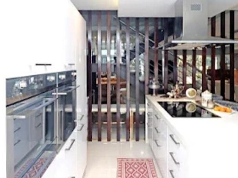 Modern kitchen featuring a central island with induction hob, stainless steel extractor fan, and built-in double ovens, separated by a decorative timber slat screen.