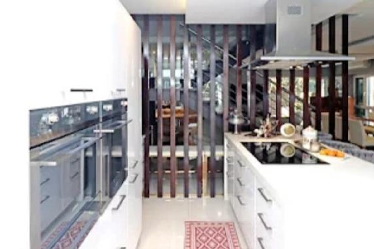 Modern kitchen featuring a central island with induction hob, stainless steel extractor fan, and built-in double ovens, separated by a decorative timber slat screen.