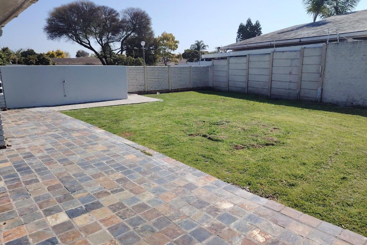 A spacious rear garden featuring a paved patio area, a well-defined lawn, and secure precast concrete boundary walls.
