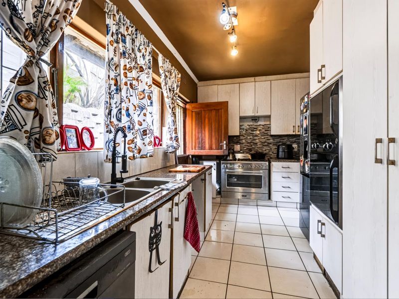 A functional kitchen featuring built-in cabinetry, granite countertops, a double basin sink, and integrated appliances with a mosaic tile backsplash.