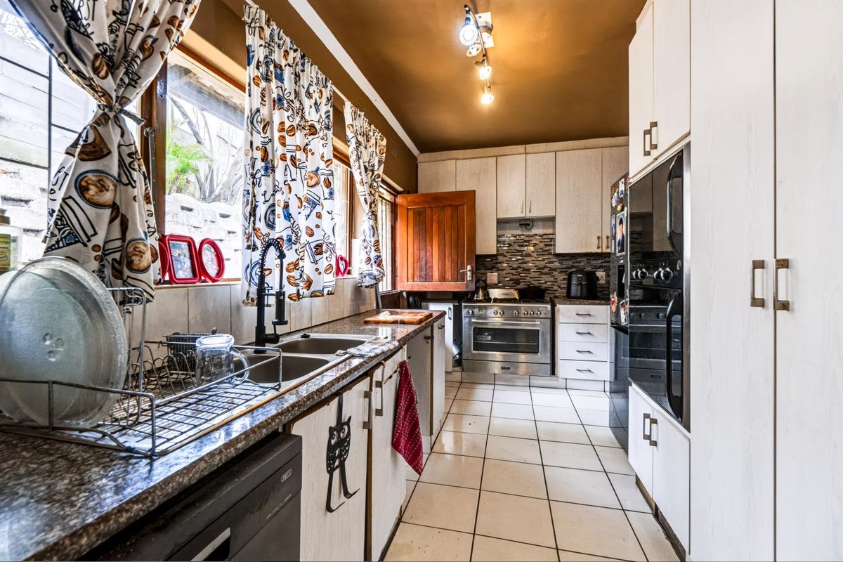 A functional kitchen featuring built-in cabinetry, granite countertops, a double basin sink, and integrated appliances with a mosaic tile backsplash.
