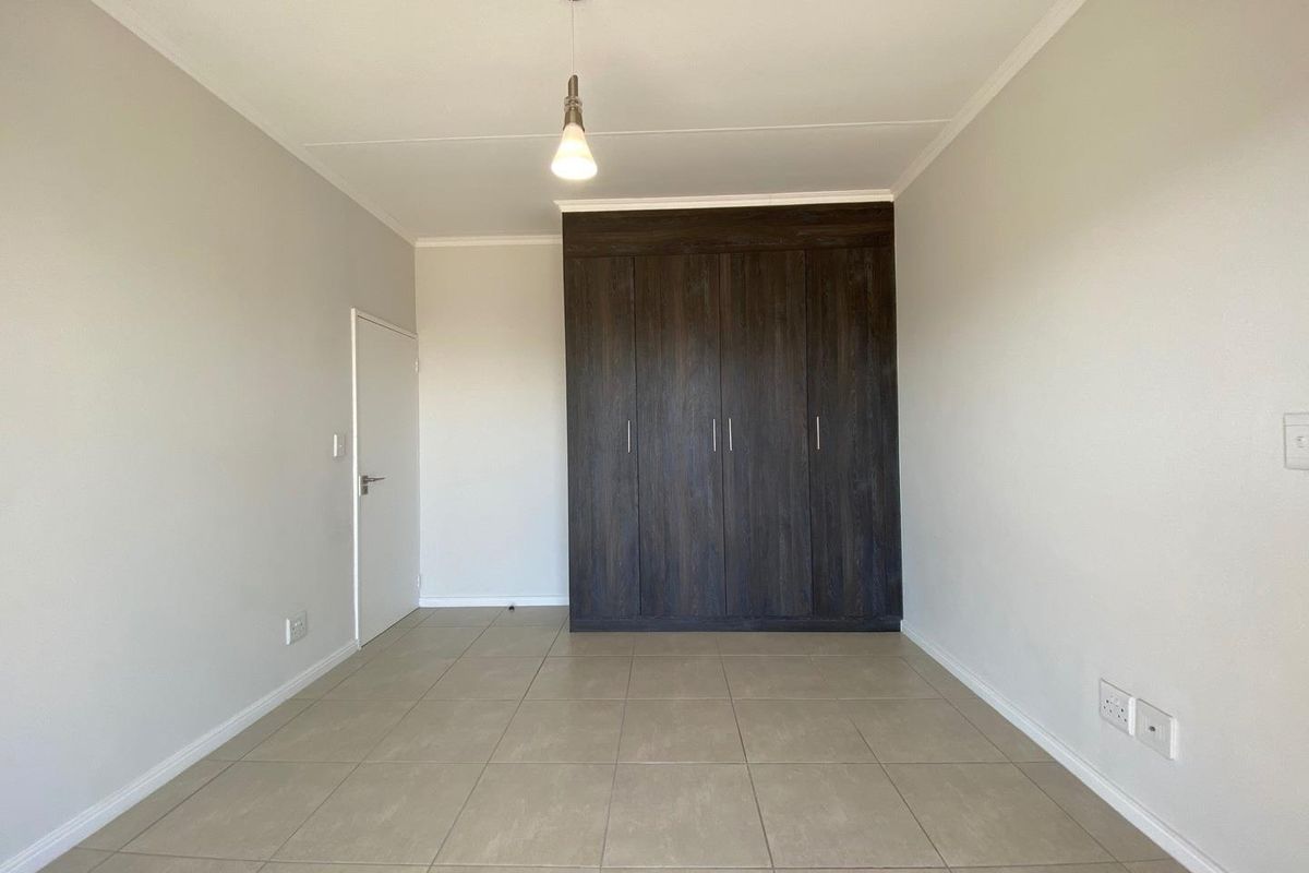A bright, empty bedroom featuring neutral tiled flooring, a modern pendant light, and dark wood built-in cupboards.