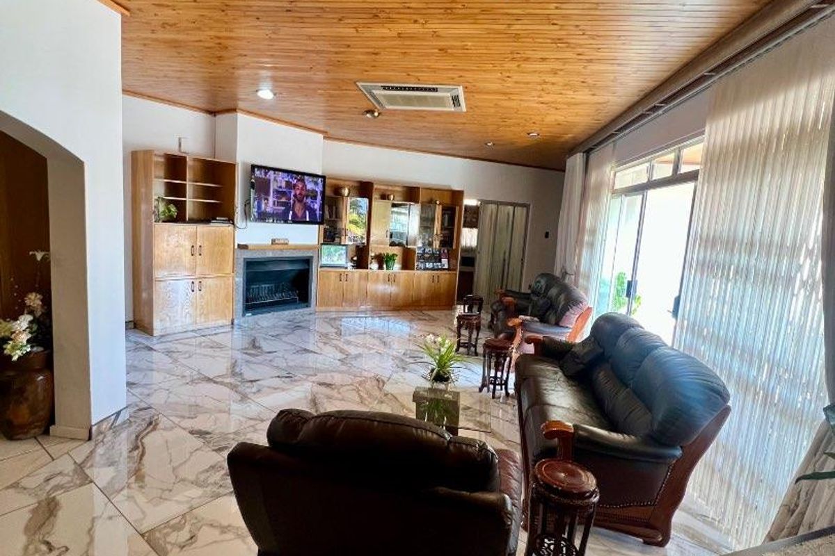 Spacious living room featuring polished marble-look floor tiles, a warm timber tongue and groove ceiling, built-in cabinetry, and a fireplace with direct patio access.