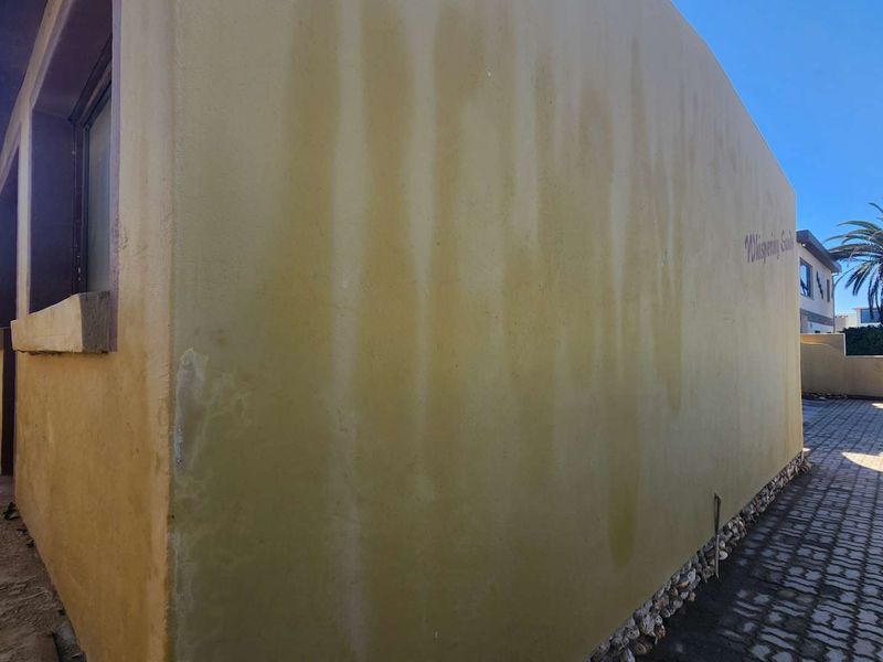 Side view of the property showing a paved driveway and an exterior wall with visible water staining and paint discoloration.