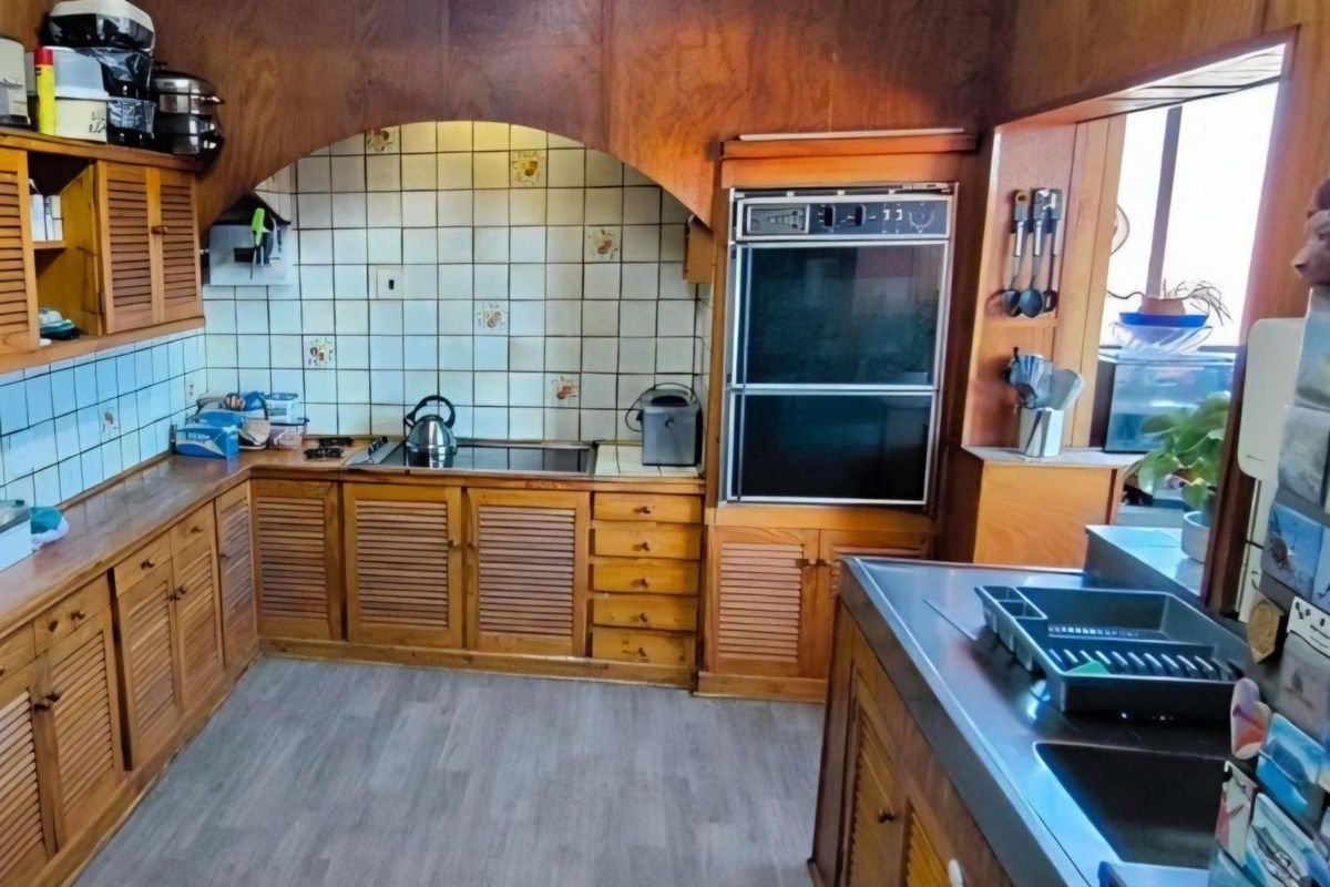 A dated kitchen featuring original wooden cabinetry, a built-in double oven, and tiled backsplash, offering significant potential for a modern renovation.