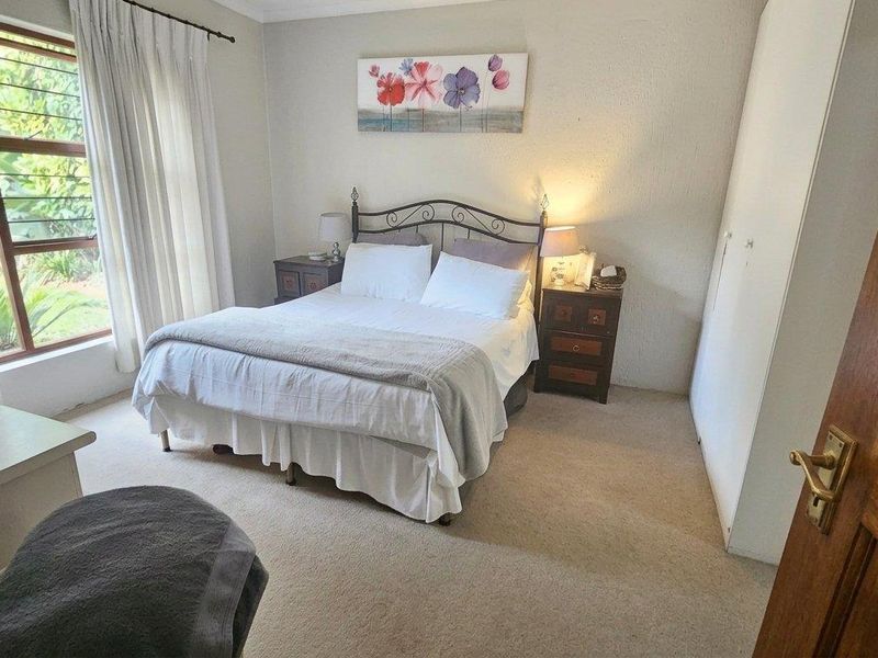 A comfortable bedroom featuring neutral carpeting, built-in cupboards, and a large window providing natural light.