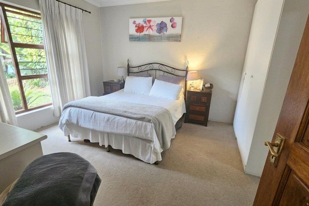 A comfortable bedroom featuring neutral carpeting, built-in cupboards, and a large window providing natural light.