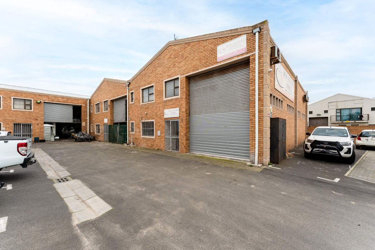 Front elevation of a commercial office and warehouse facility featuring brick construction, multiple roller shutter doors, and paved parking area.