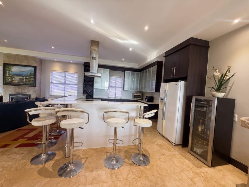 Modern open-plan kitchen featuring a central island with breakfast bar seating, dark cabinetry, and integrated appliances, seamlessly flowing into the living area.