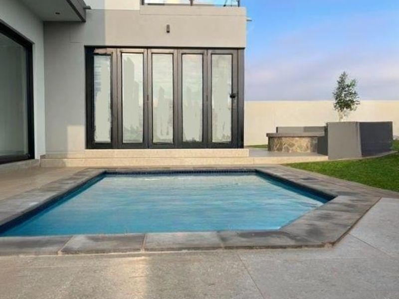 Modern outdoor pool area featuring stone paving, a built-in seating area, and large bi-fold doors leading into the main residence.