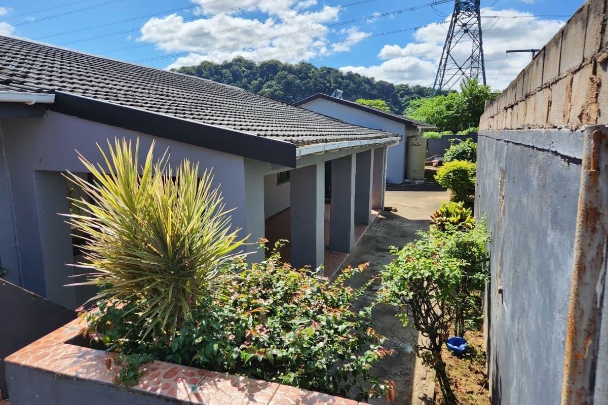 Rear exterior view of the property featuring a covered patio area, paved walkway, and boundary wall with a water tank.