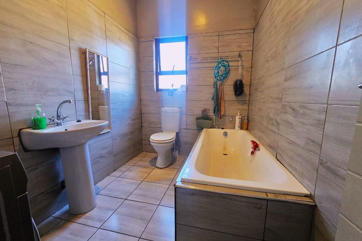 A functional bathroom featuring a pedestal basin, toilet, and built-in bathtub with full-height wall tiling and tiled flooring.