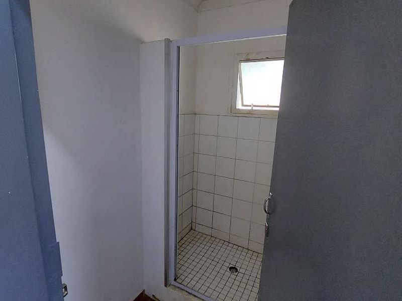 A compact bathroom featuring a tiled shower enclosure and tiled flooring, currently in need of cosmetic updates and maintenance.