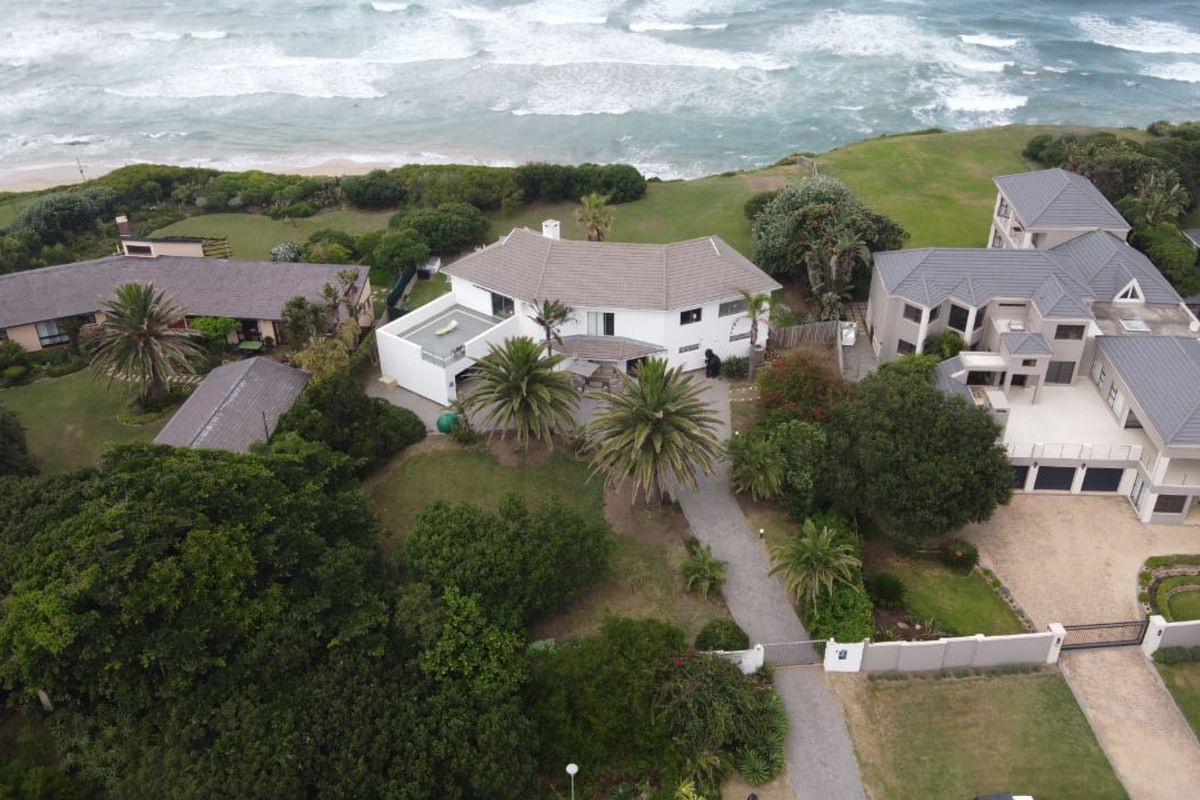 Aerial view of a coastal residential property featuring a large main house, expansive garden, paved driveway, and direct proximity to the ocean.