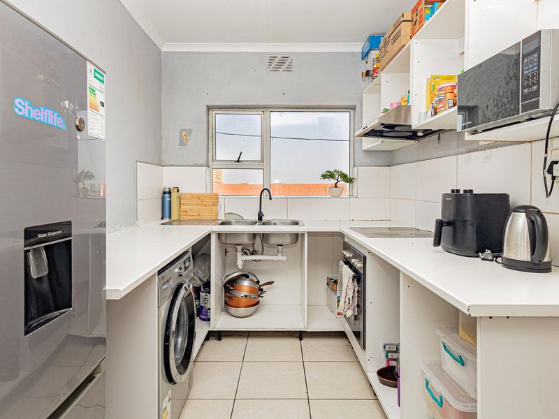 Compact kitchen featuring built-in oven, hob, extractor fan, and double sink, with open shelving and tiled finishes throughout.