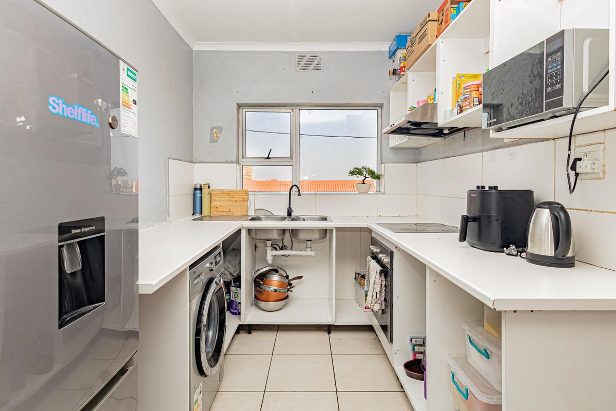 Compact kitchen featuring built-in oven, hob, extractor fan, and double sink, with open shelving and tiled finishes throughout.