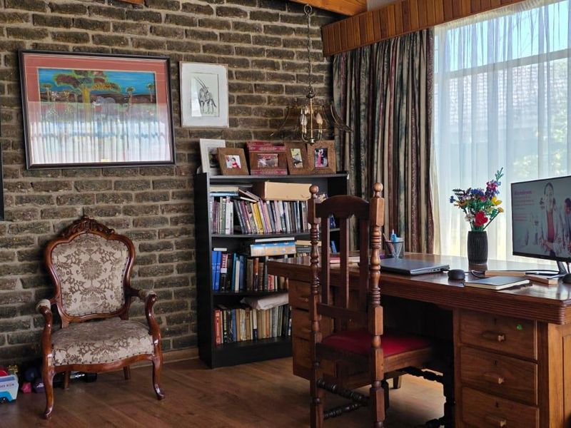 A home office featuring a rustic exposed brick wall, timber flooring, and large windows that provide ample natural light.