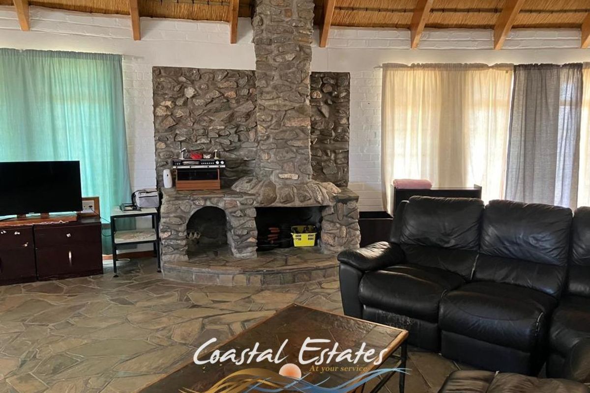 Spacious living area featuring a prominent natural stone fireplace, exposed thatch roof beams, and rustic stone flooring.