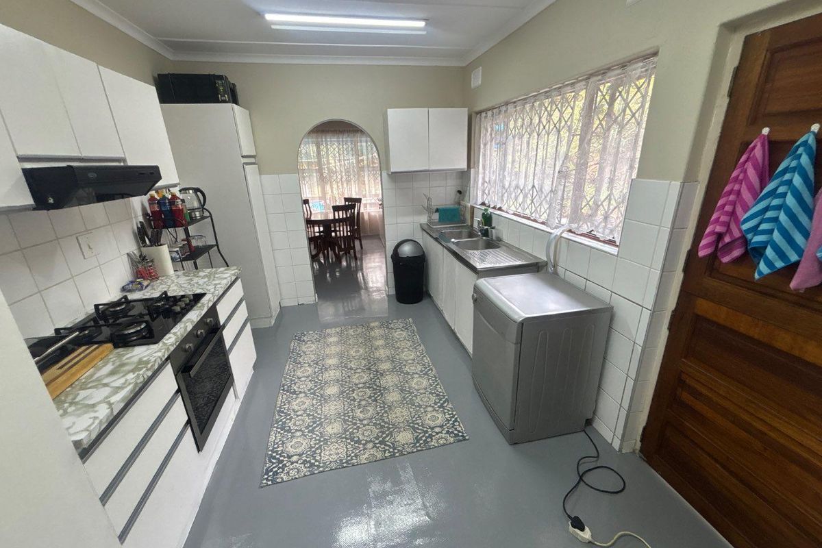 A functional kitchen featuring white cabinetry, a gas hob, built-in oven, and tiled splashbacks, with an arched doorway leading to the dining area.