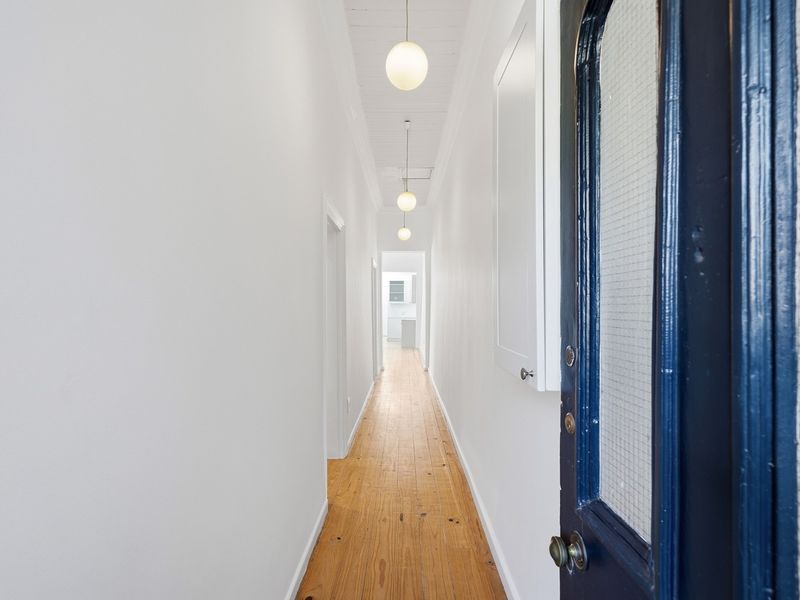 A bright, clean hallway featuring polished timber flooring, a classic beaded board ceiling, and modern pendant lighting, leading towards the rear of the home.