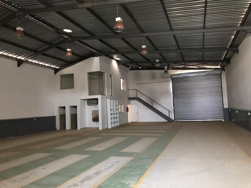 Spacious industrial warehouse featuring high ceilings with exposed steel trusses, a large roller shutter door, mezzanine level, and durable concrete flooring.
