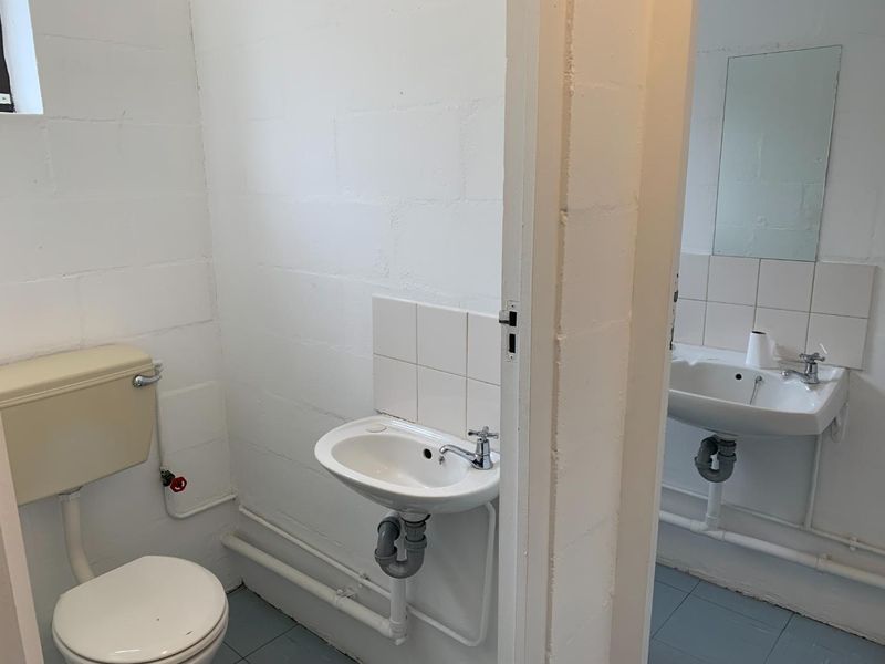 A functional bathroom featuring basic sanitary ware, exposed plumbing, and painted concrete block walls, offering potential for modernization and cosmetic upgrades.