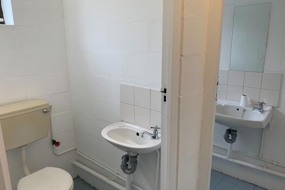 A functional bathroom featuring basic sanitary ware, exposed plumbing, and painted concrete block walls, offering potential for modernization and cosmetic upgrades.