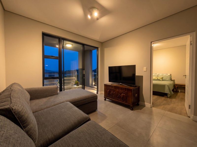 A well-maintained living room featuring large sliding glass doors leading to a balcony, neutral tiled flooring, and recessed ceiling lighting.
