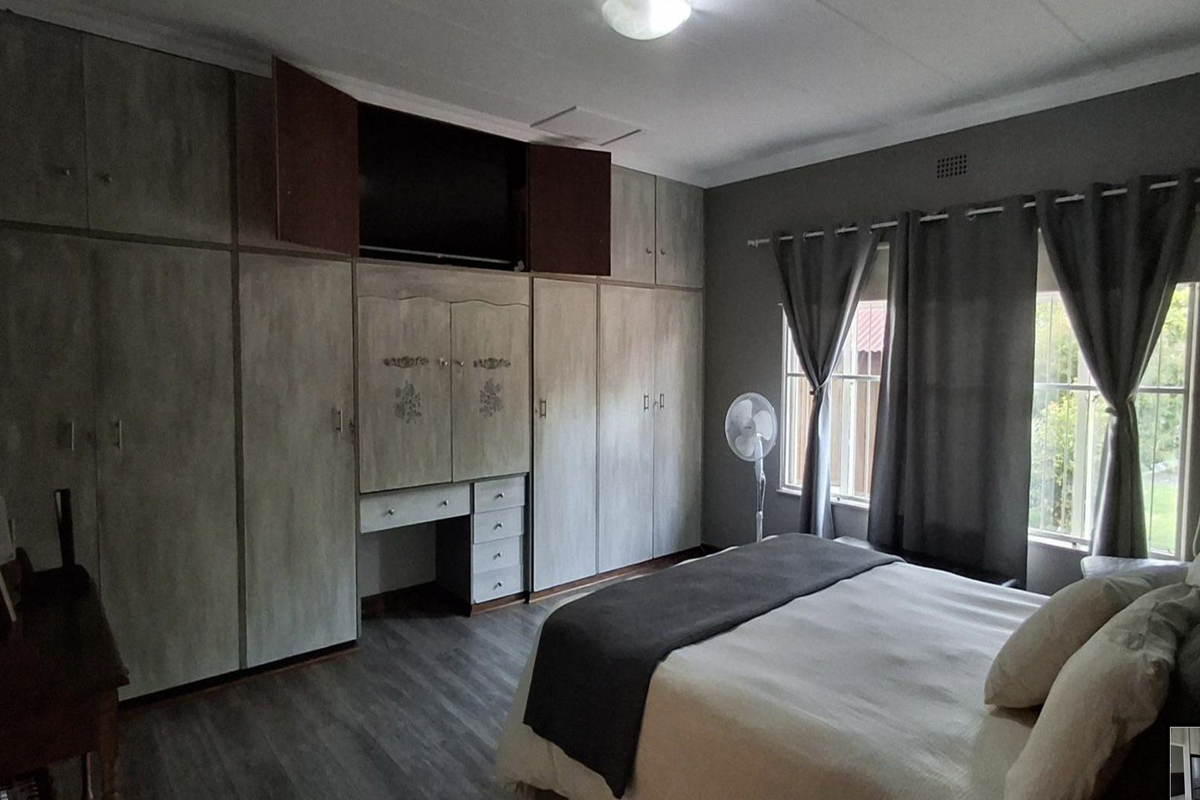 A bedroom featuring extensive built-in cabinetry with integrated vanity and storage, complemented by grey wood-look flooring and neutral wall tones.