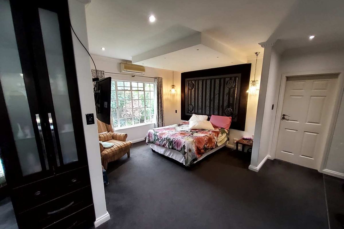 A spacious bedroom featuring a recessed ceiling with downlights, built-in wardrobe, and an integrated air conditioning unit.
