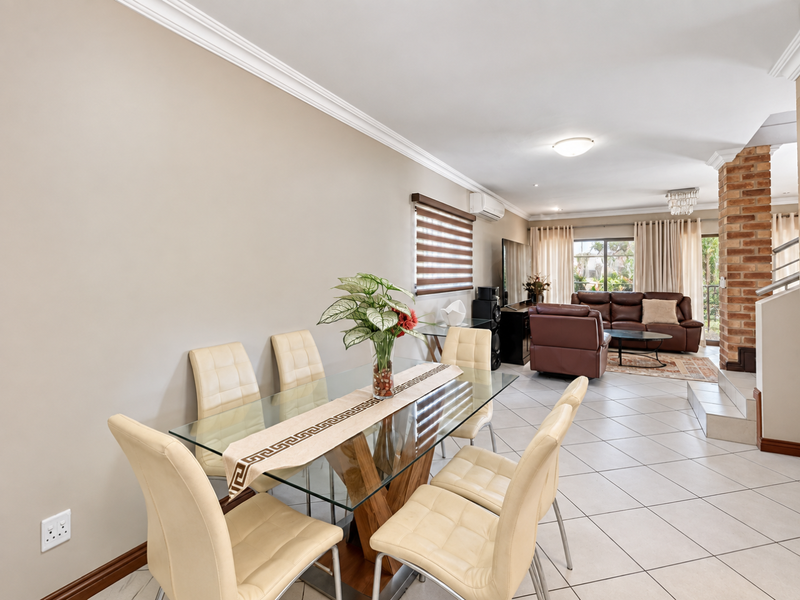 Spacious open-plan living and dining area featuring ceramic floor tiles, crown molding, and an exposed brick feature pillar leading to the staircase.
