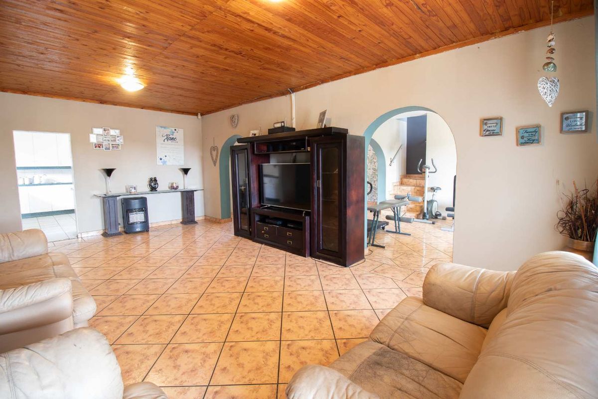 Spacious living room featuring a timber-clad ceiling, ceramic tiled flooring, and an arched entryway leading to an adjacent area.