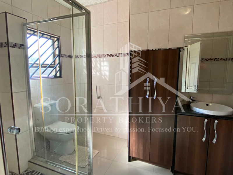 A modern bathroom featuring a glass shower enclosure, vanity cabinet with basin, wall mirror, and neutral tiled finishes.