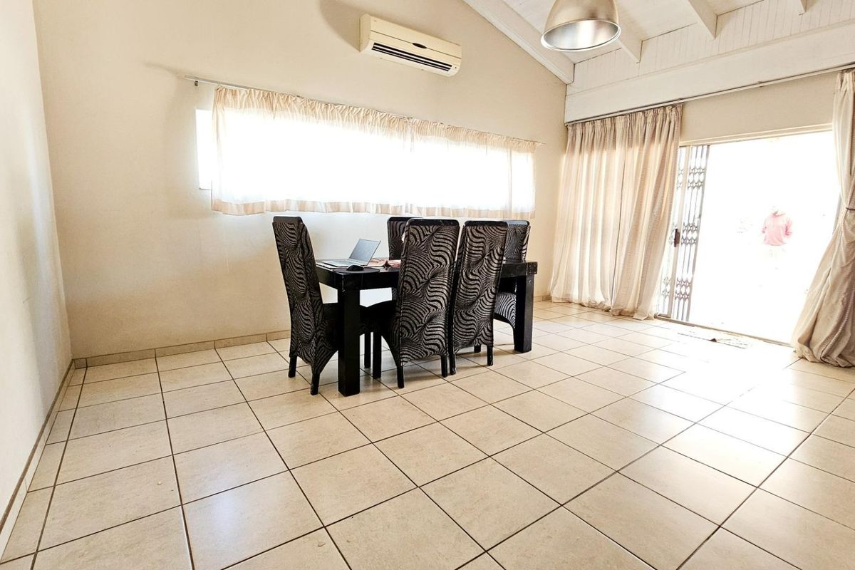 Spacious living area featuring tiled flooring, vaulted ceilings, and a wall-mounted air conditioning unit, with direct access to the outdoor area.