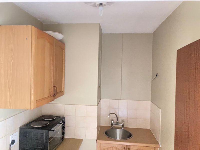 A compact kitchen area featuring built-in wooden cabinetry, a stainless steel sink, and a tiled backsplash, offering a functional but dated space.
