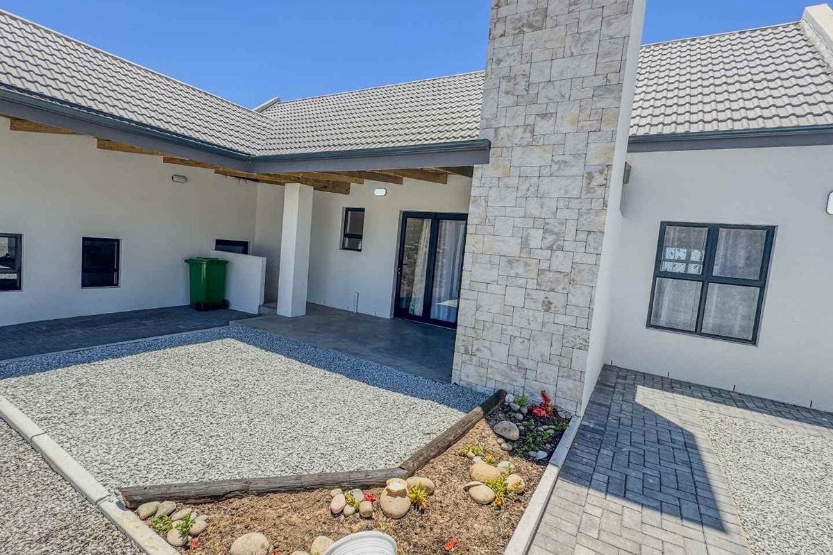 A well-maintained rear exterior view featuring a covered patio, stone-clad chimney, paved pathways, and a landscaped garden area with gravel.