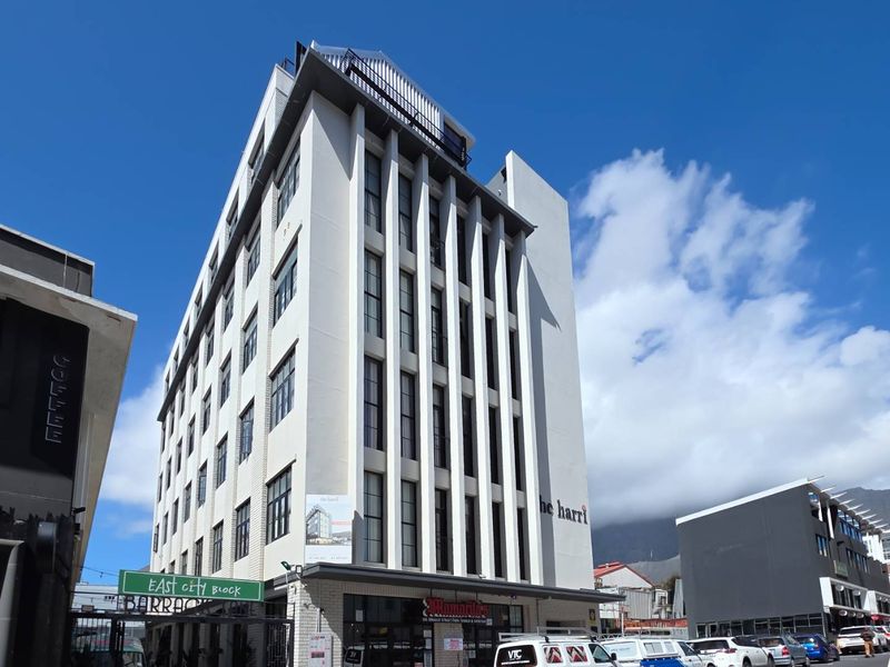 A modern multi-story apartment building facade featuring large windows, a ground-level commercial storefront, and a rooftop terrace area.