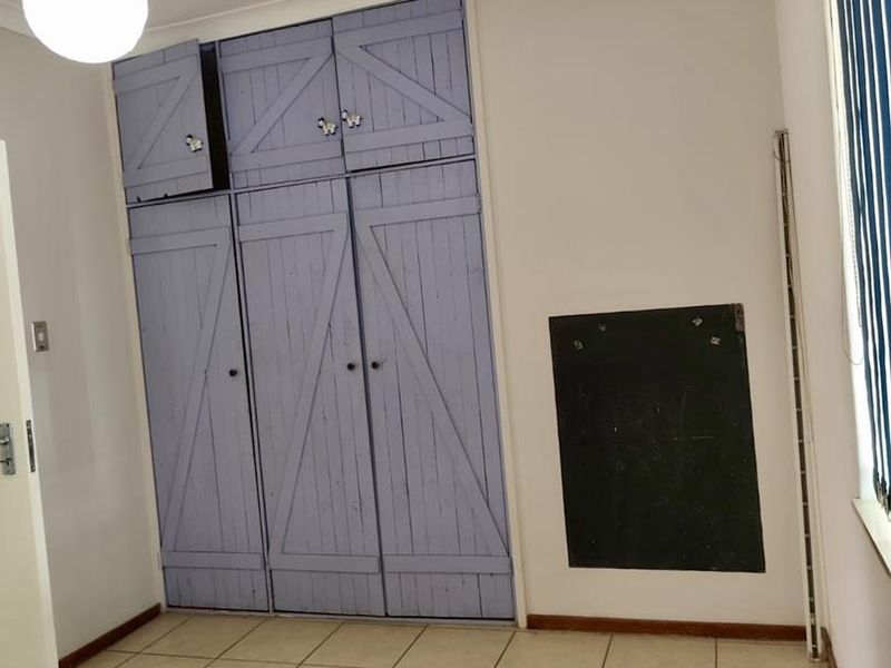 A vacant bedroom featuring tiled flooring, built-in cupboards with a painted finish, and vertical window blinds.