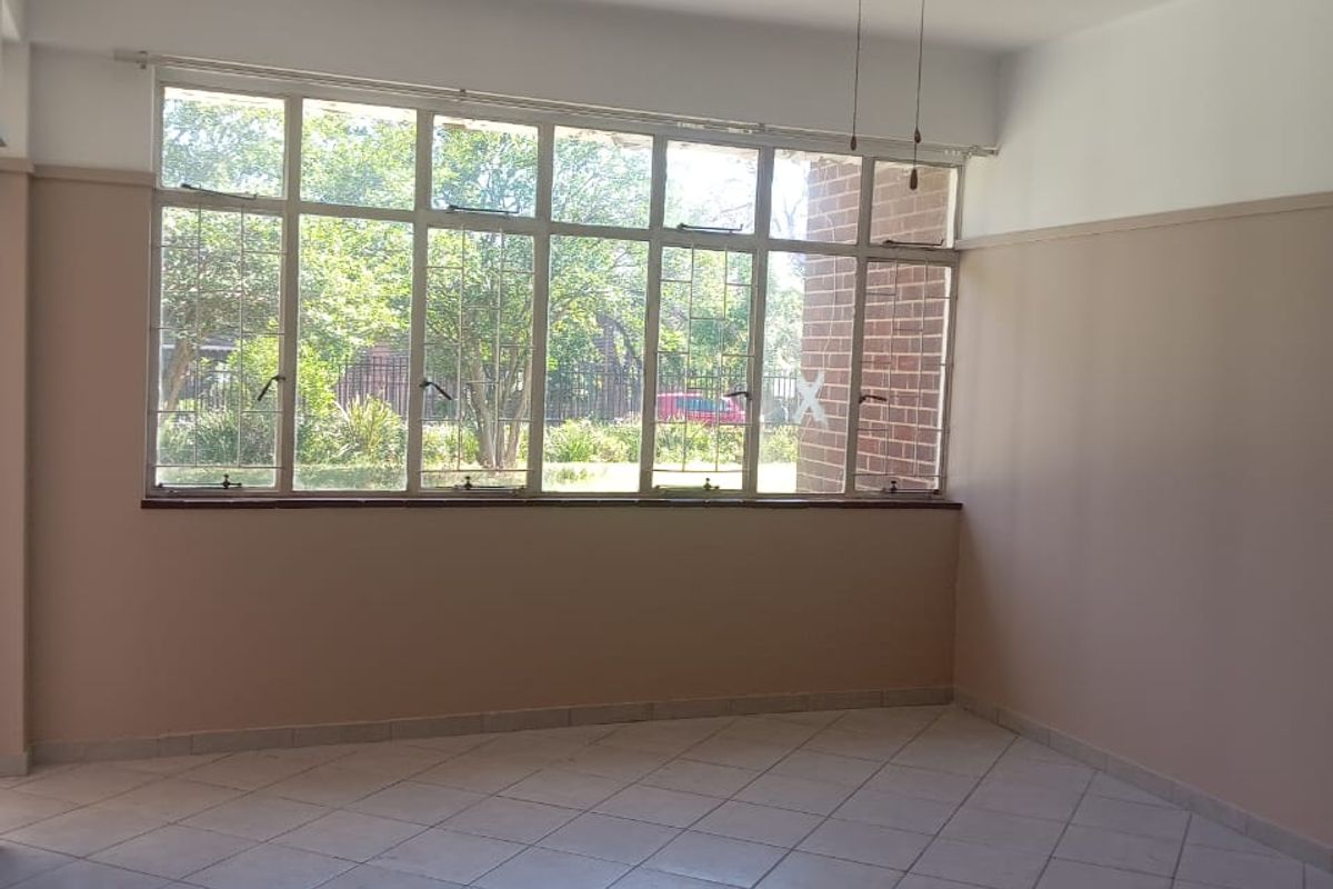 An empty living room featuring tiled flooring, a ceiling fan, and large windows providing natural light and garden views.