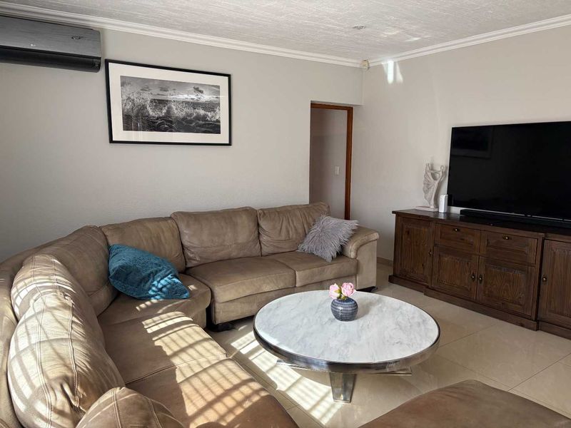 A comfortable living room featuring tiled flooring, coved ceilings, and a wall-mounted air conditioning unit.