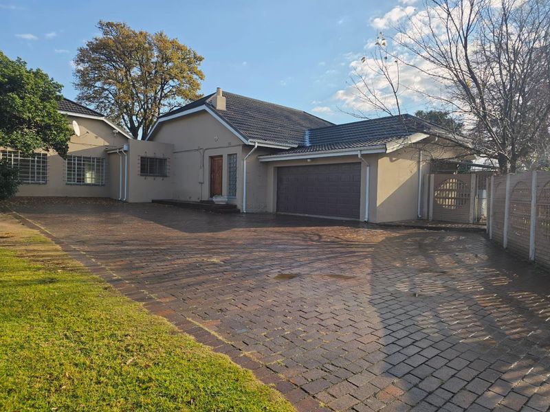 Front view of a single-story house featuring a large paved driveway, double garage, and secure perimeter walling.
