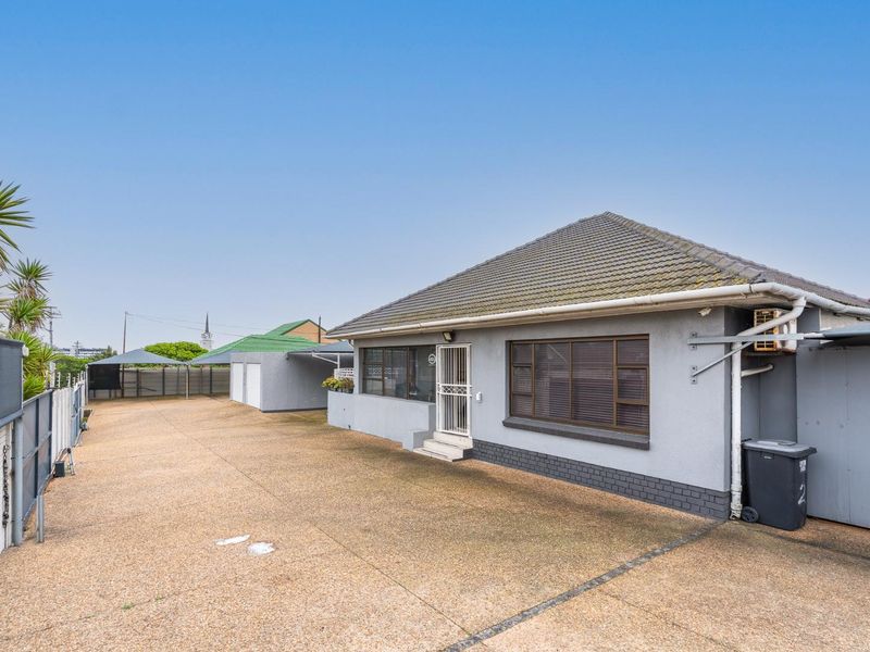 Front exterior view of the house featuring a large concrete driveway, tiled roof, and secure gated entrance with ample parking space.